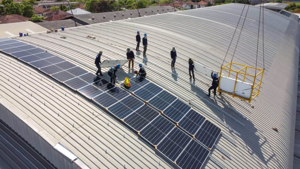 Solar panel installers working on a curved warehouse roof